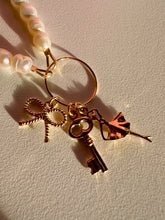 Load image into Gallery viewer, Woman pearls necklace with gold plated elements such as: round connector, bow pendant, ballerina pendant and key pendant.